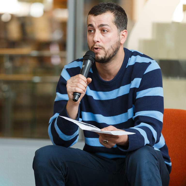 A student talks on a microphone to a group about his Capstone project. 